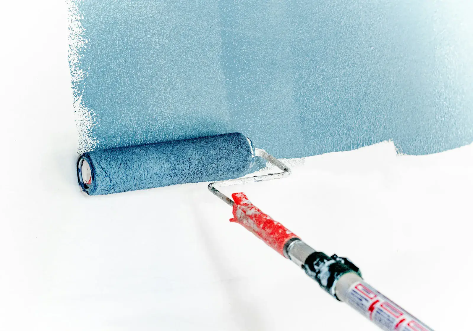 Rouleau de peinture appliquant une couche de bleu sur un mur blanc